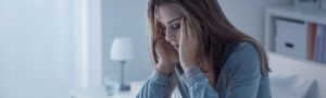 A distressed woman sitting on a bed, holding her head in her hands