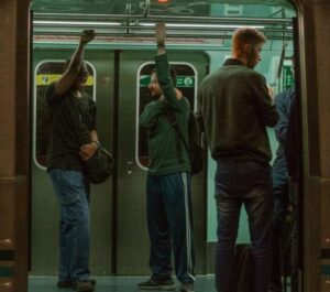 Passengers standing inside a subway train, gripping onto handrails